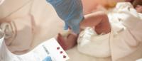 a medical professional collecting blood spots from heel of infant